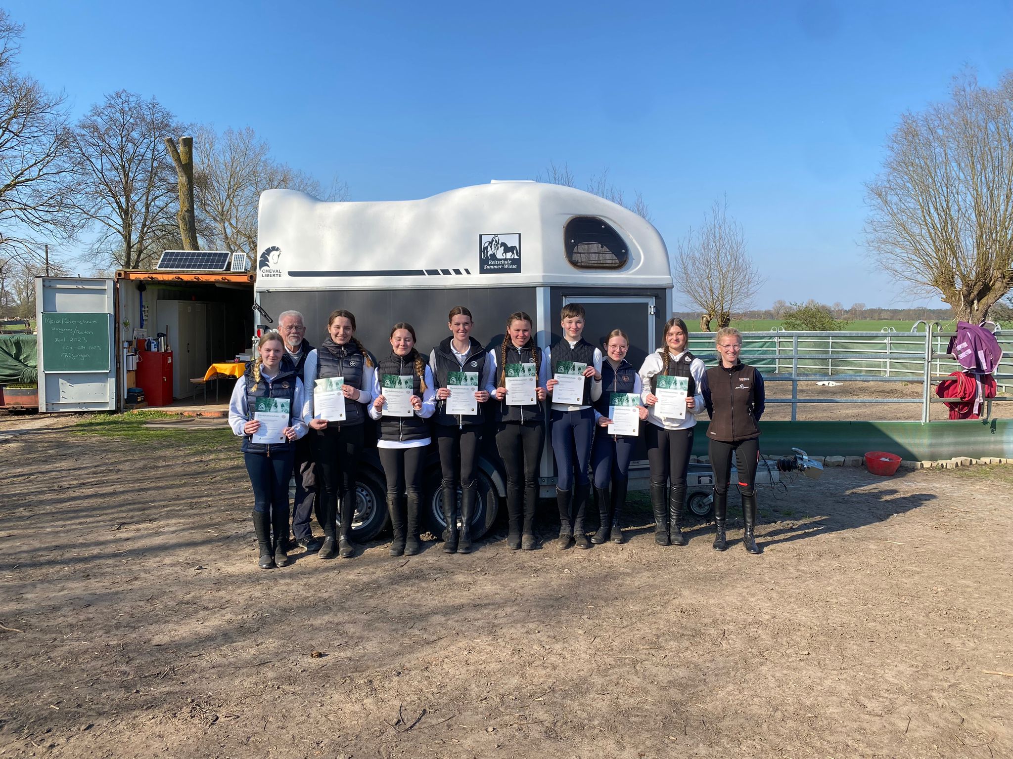 Gruppe von Reitschülerinnen und Reitschülern mit bestandenen Prüfungsurkunden vor dem Pferdeanhänger der Reitschule Sommerwiese